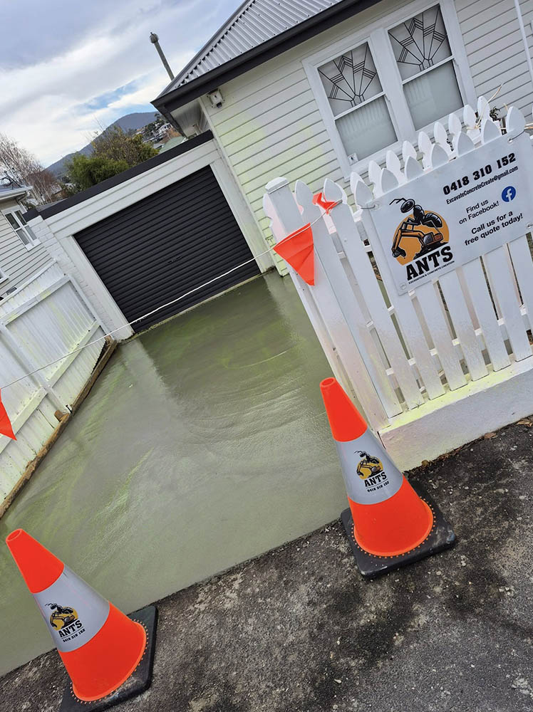 Freshly poured concrete driveway behind traffic cones and a company sign on the fence