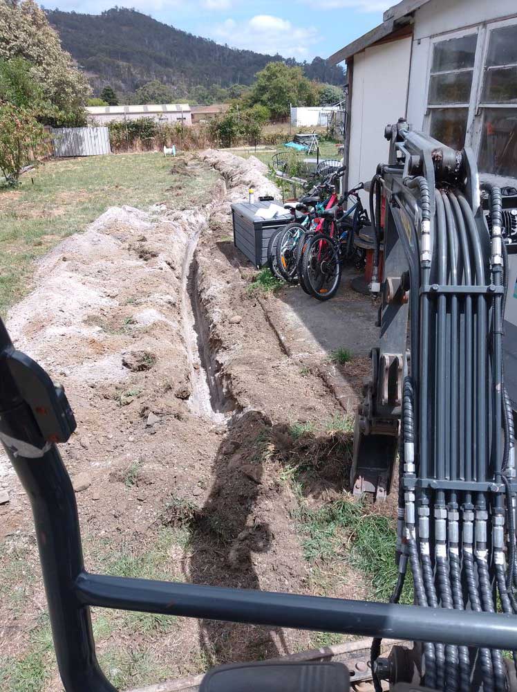Trench dug beside a house, seen from an excavator cab