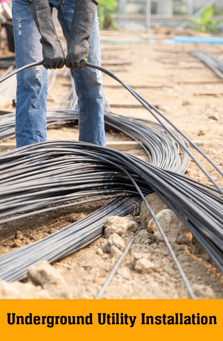 Worker in gloves pulling bundles of black cable across dirt, labelled Underground Utility Installation