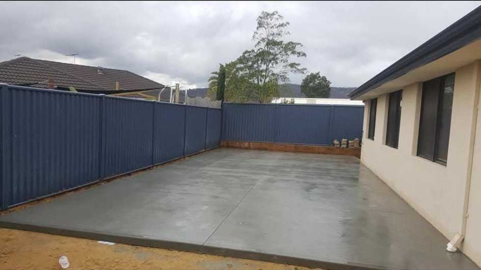 Large new concrete slab in a fenced backyard beside a house