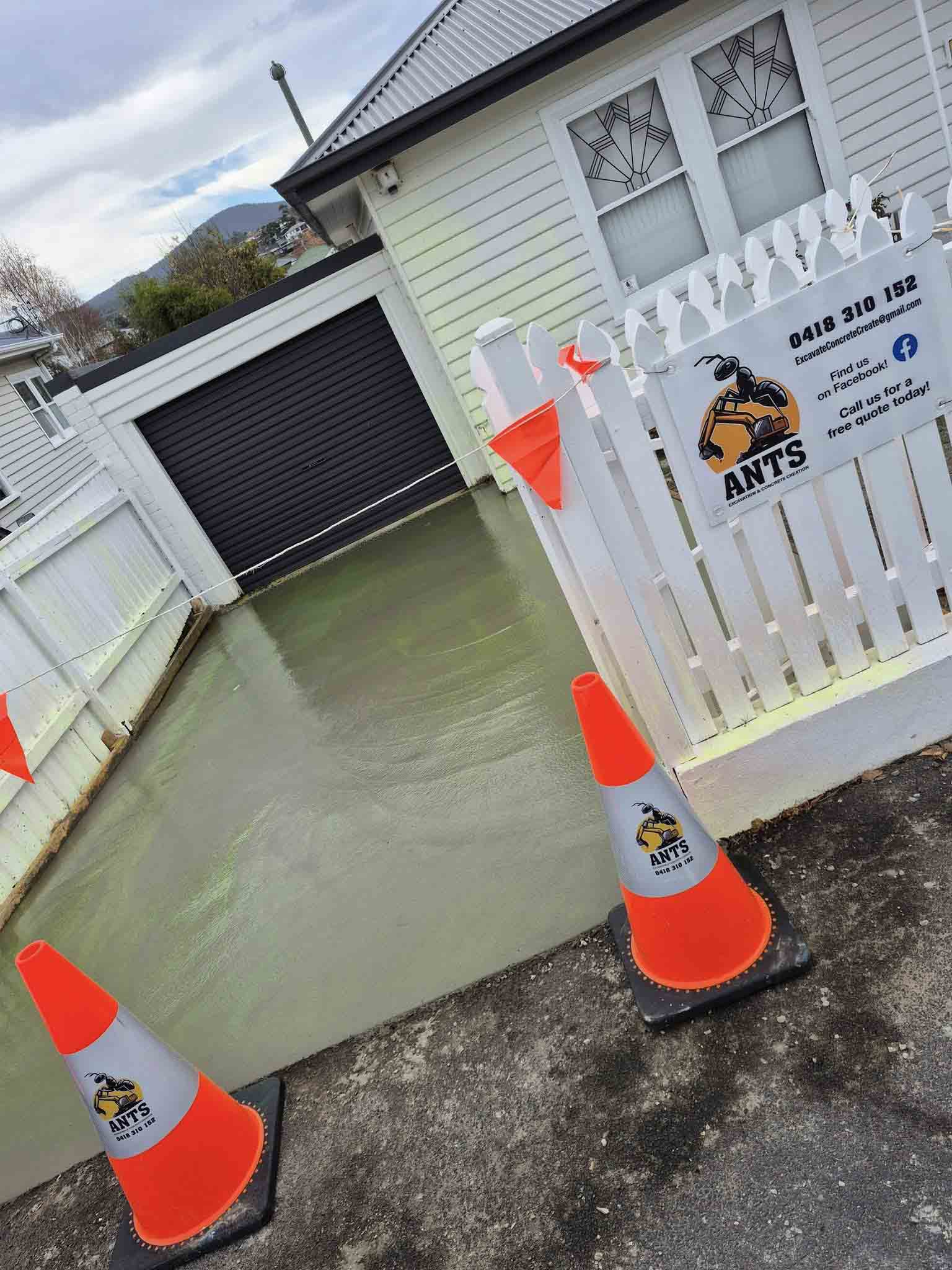 Freshly poured concrete driveway behind traffic cones and a company sign on the fence