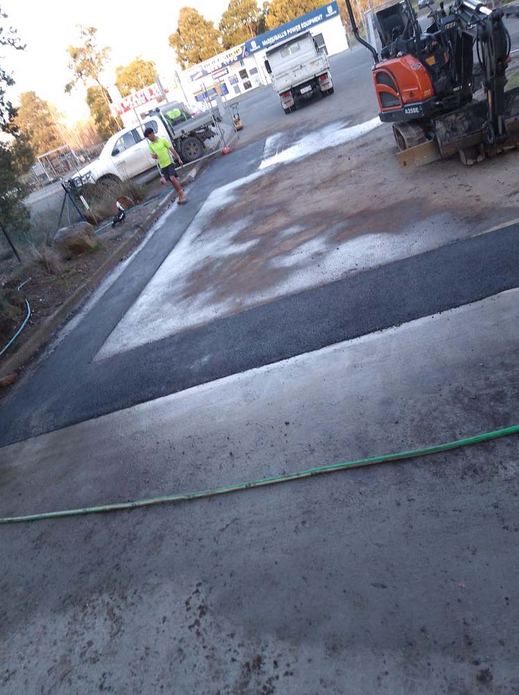 New concrete strip beside asphalt with an excavator behind
