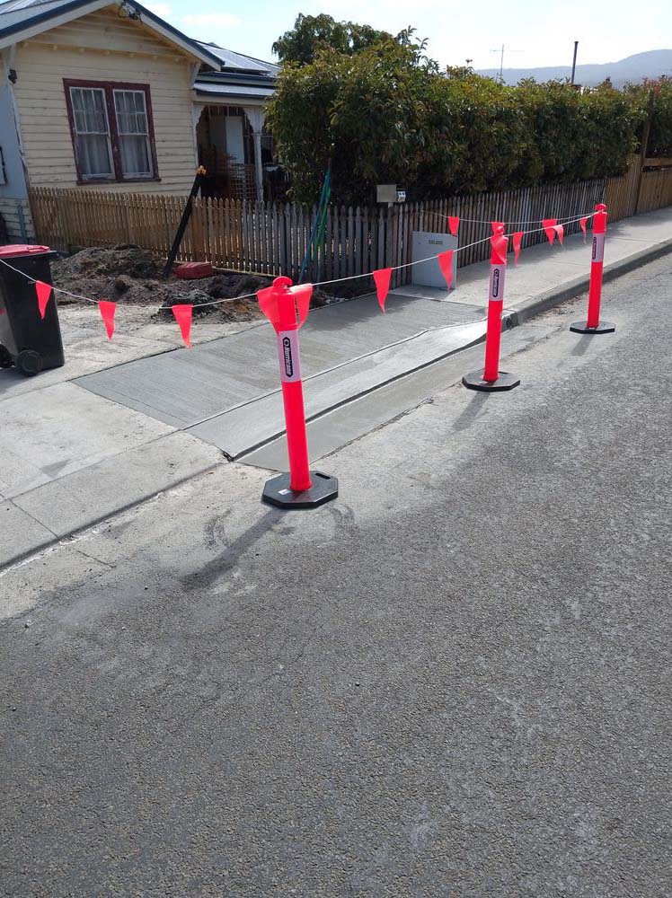 New concrete footpath fenced off with orange barriers outside a house