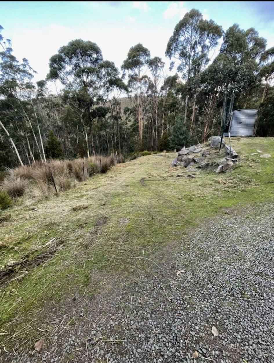 Cleared grassy block with a gravel area, rock pile and gum trees