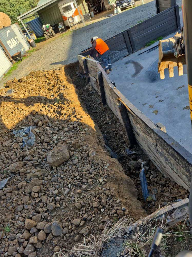Deep trench dug beside a concrete slab with a worker in hi-vis