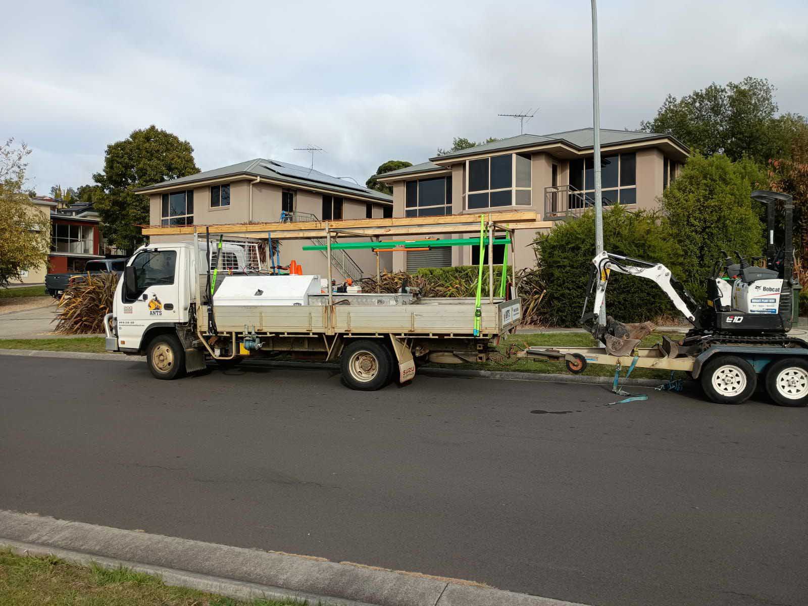 Tray truck towing a mini excavator on a trailer in a suburban street