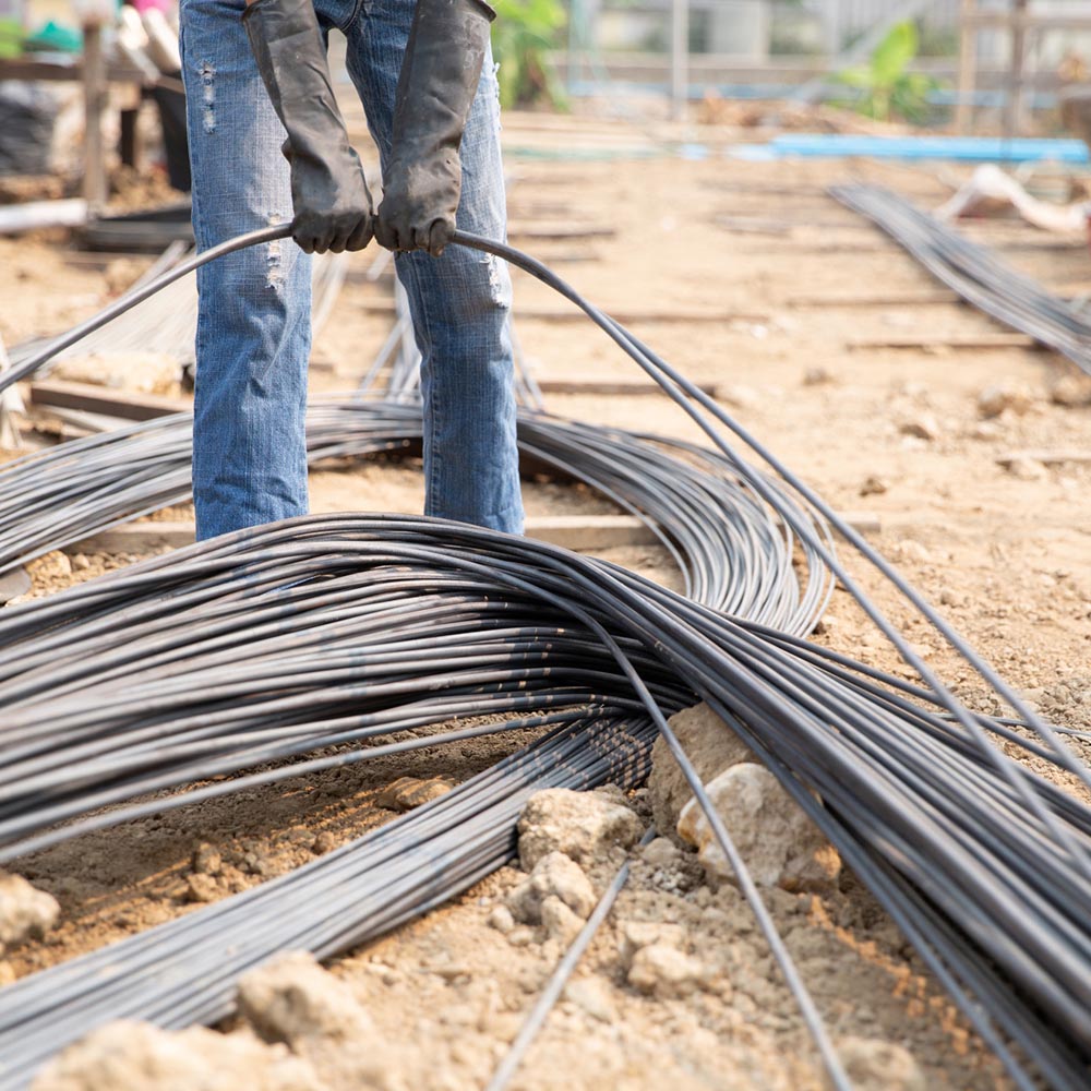 Worker in gloves pulling bundles of black cable across dirt