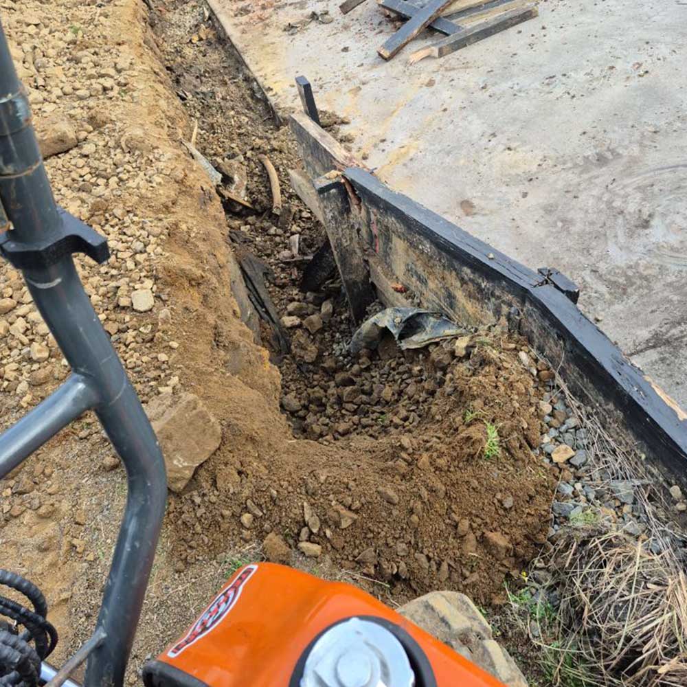 Trench dug along a concrete slab edge, seen from an excavator